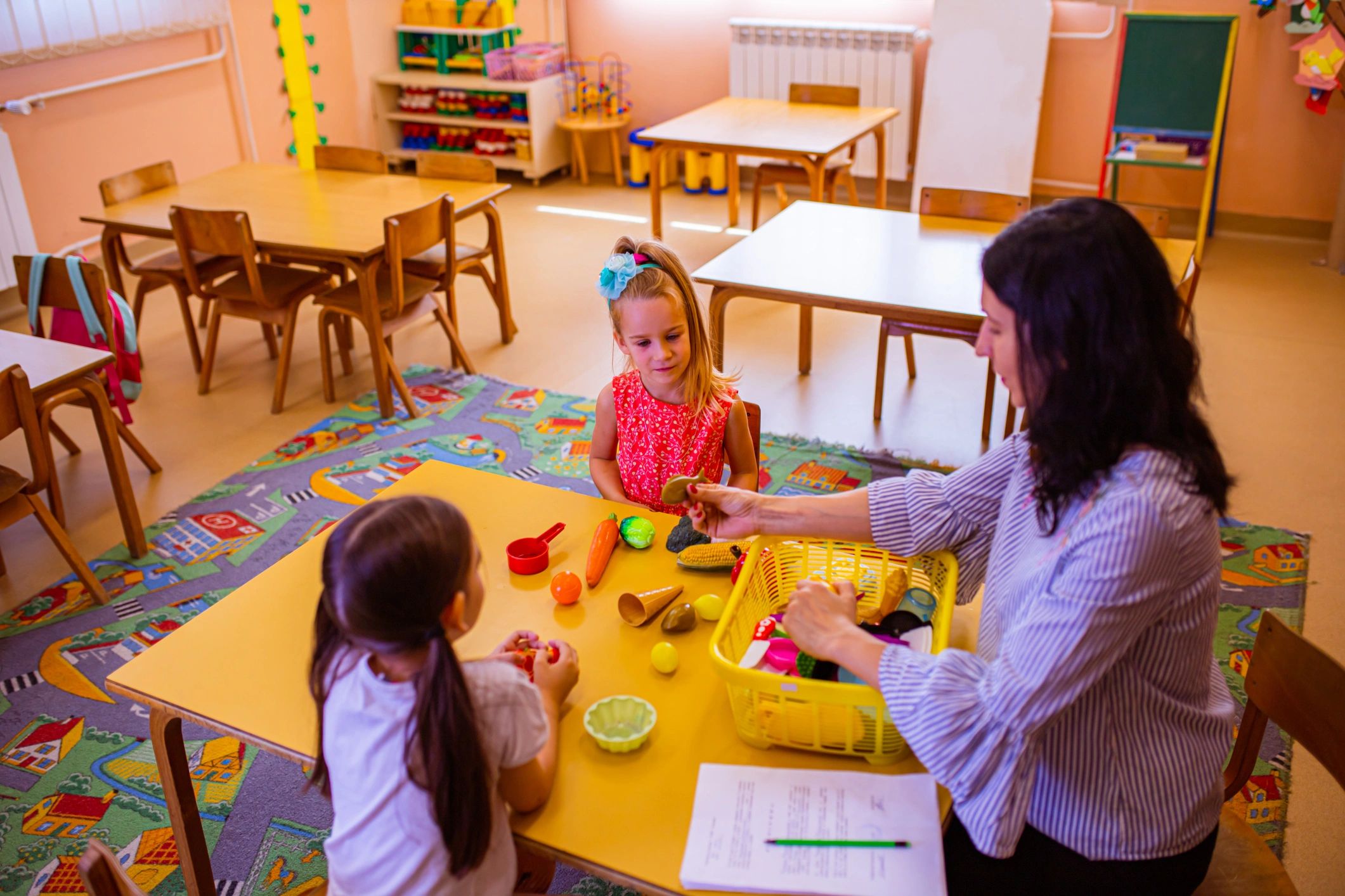 Preschool children building with colorful blocks with a teacher nearby